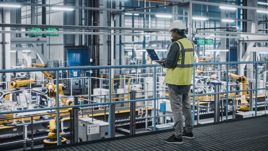 Engineer using laptop on factory floor in liquid product manufacturing facility